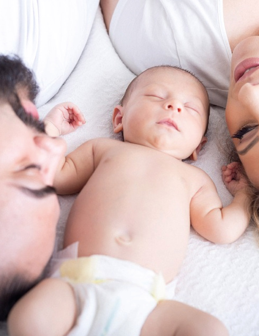 family lying on bed with newborn baby in the middle
